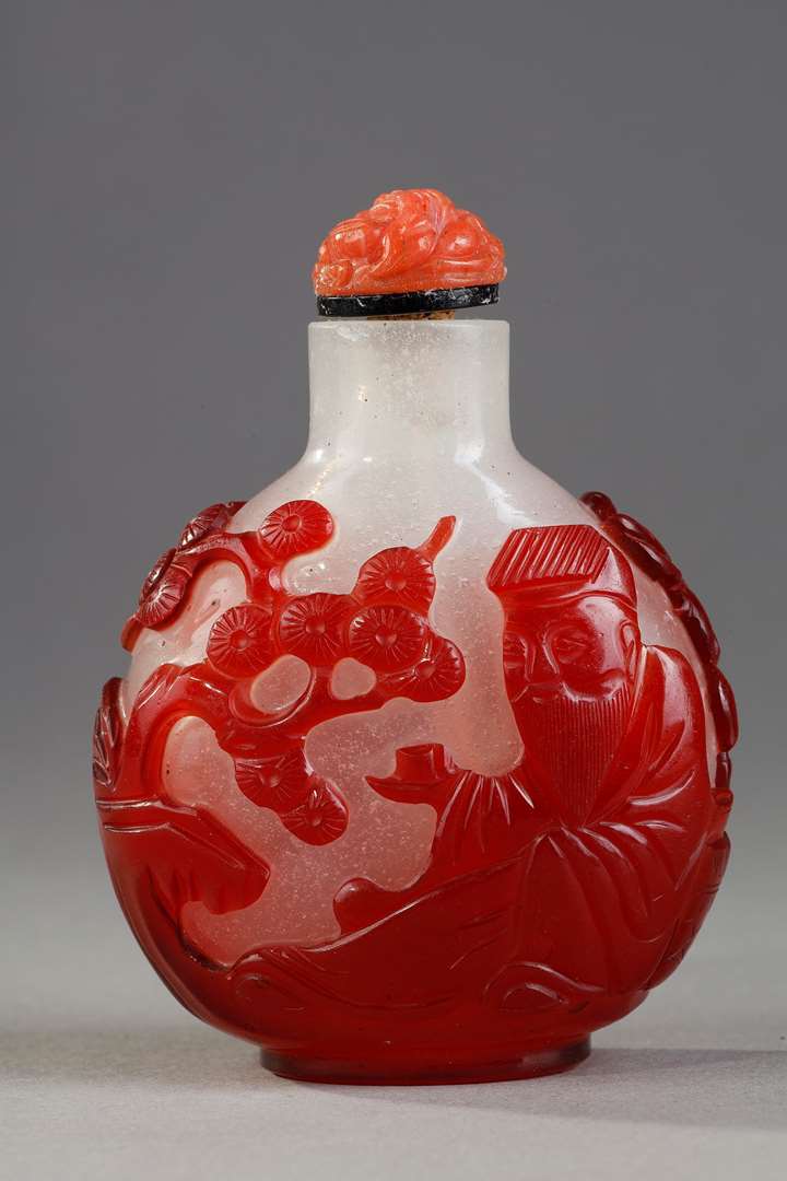 Snuff bottle  red overlay glass with Shou Lao holding a peche of longevity and looking at peches and on the other side of a character holding a cup on a tray in front of a pine - China 1800/1850